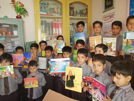 Boys in a classroom in Pakistan holding up books from an Alif Laila box library